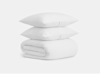 Two white pillows are stacked on top of a neatly folded white comforter, all set against a plain white background. The bedding appears soft and clean.