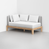 A minimalist daybed with a light wooden frame, gray upholstered backrest, and three white pillows, positioned in the corner of a room with plain white walls and a light gray floor.