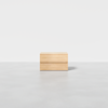 A minimalist wooden box with clean lines sits centered on a smooth, light gray floor against a plain white background.