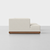Side view of a modern, light beige upholstered sofa with a low back and seat, featuring a wooden base, placed on a plain light gray floor against a white background.