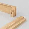 Two pieces of light wood with precisely cut interlocking joints, positioned on a smooth, light gray surface, appear ready to be assembled together.