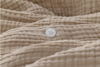 A close-up of beige, textured, crinkled fabric with a single white, four-hole button sewn onto it. The button is centered among the fabric folds.