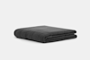 A neatly folded, dark gray quilt or blanket lies on a plain, light gray background.