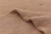 A close-up of a textured, light brown or beige fabric with a crinkled, quilted pattern. One part of the fabric is slightly lifted, showing its soft and flexible nature.