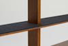 A close-up view of a wooden shelving unit with a vertical support intersecting a horizontal shelf covered in a dark gray felt material, set against a plain light background.
