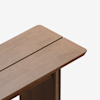 A close-up view of the corner of a wooden table with a smooth surface and a narrow gap running along the center. The table has a minimalist design and light brown finish.