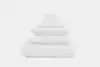 A neatly stacked set of white bedding essentials, including a comforter, pillows, and folded sheets and towels, arranged in descending size order against a plain white background.