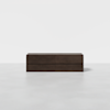 A modern, dark wood dresser with four drawers standing on a light, smooth floor against a plain white background.