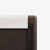 Close-up of the corner of a dark wooden bed frame with a rounded edge and a white fabric cover draped over the top rail, against a plain white background.