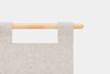 A close-up of a light gray felt fabric hanging from a smooth wooden rod, with two fabric loops securing it. The background is plain white.