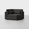A modern, dark gray corner chair with thick cushions and a matching lumbar pillow, set against a plain light gray background. The chair has clean lines and a boxy, contemporary design.