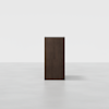 A dark brown wooden cabinet with clean, simple lines stands alone on a light gray, empty floor against a plain white background. The cabinet is viewed from the front.