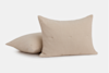 Two beige rectangular pillows with a soft, textured fabric are placed on a plain white background, with one pillow standing upright and the other lying flat behind it.