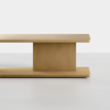 A minimalist wooden table with a rectangular top and base, connected by a central, vertical support panel, all in a light natural wood finish, set against a plain white background.