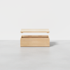 A light wooden storage box with a hinged lid partially open, placed on a smooth gray surface against a plain white background.