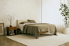 Minimalist bedroom with a wooden bed, neutral bedding, and matching pillows. A wooden nightstand with decor sits next to the bed. Large potted plant and sheer curtains complete the airy, serene space.