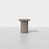A minimalist, square-top side table with rounded edges and a cylindrical base, made of light brown wood, set against a plain white background.