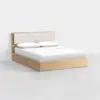 A modern wooden bed frame with a light wood finish, featuring a padded beige headboard. The bed is neatly made with white sheets, a white blanket, and two white pillows. The background is plain and minimalistic.