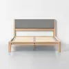 A modern wooden bed frame with a light wood finish, slatted base, and a rectangular gray upholstered headboard, set against a plain white wall and floor.