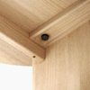 Close-up view of the underside of a light wood table, focusing on the corner joint where two pieces meet and are secured by a visible black screw. The wood grain and smooth finish are clearly visible.