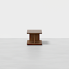 A small, square wooden table with a minimalist design, featuring a thick top and base connected by a central support, set against a plain white background.