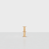 A small, light wood side table with a minimalist design, featuring two shelves, stands alone on a light gray floor against a plain white background.