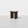 A modern, minimalist wooden stool with wide legs and a beige cushioned seat, set against a plain white background.