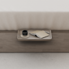 A wooden tray on a wooden bench holds a black cup on a saucer, an open notebook, and a pen. The bench sits at the foot of a bed with a cream-colored blanket.