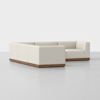 A modern, cream-colored sectional sofa with a low wooden base, arranged in an L-shape on a light gray floor against a plain white background.