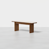 A minimalist wooden bench with a rectangular seat and sturdy legs, featuring a light-colored cushioned top, placed in a plain, light gray setting.