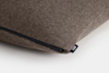 A close-up of a soft, brown fabric pillow with a black zipper and a small tag that reads Thuma on a white background.