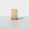 A square, light wood planter box with four short cylindrical legs, positioned on a smooth, light gray surface against a plain white background.