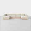 A large, U-shaped sectional sofa with light beige upholstery and a wooden base, set on a smooth light gray floor against a plain white background.