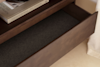 An open wooden drawer is empty below a shelf holding books, one titled PORTRAITS OF HOME | DISC INTERIORS. The furniture sits on a light-colored floor next to a beige wall and a curtain.