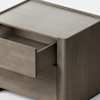 A modern, light wood nightstand with clean lines is shown against a plain white background. One drawer is partially open, revealing its interior. The furniture has a minimalist and boxy design.