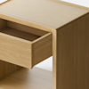 A minimalist wooden cabinet with a single drawer partially open, standing on short cylindrical legs against a plain, light background.