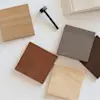 A selection of fabric swatches in neutral tones and wooden samples in various shades arranged on a white surface next to a small vase with eucalyptus stems.