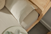 A neatly made bed with light beige sheets and a pillow, next to a small round table holding a glass and a carafe of water. The bed frame and headboard are made of light-colored wood.