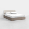 A minimalist bed with a light beige upholstered headboard, white bedding, and a wooden platform base, positioned against a plain white wall in a simple, modern room.