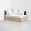 A modern daybed with a light wood frame, white mattress, and white pillows, placed against a white wall in a minimalistic, empty room with a light gray floor.