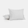 Two white pillows are placed on a white surface, with one pillow standing upright and the other lying flat behind it. The background is plain and light-colored.