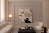 A modern living room with neutral tones features a large abstract painting, a beige sofa, a round armchair, a black coffee table with decor, a floor lamp, and sheer curtains letting in natural light.