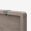 Close-up of a wooden tabletop with rounded edges, featuring a small gray metal clamp or bracket attached to the top edge against a plain white background.