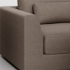 Close-up view of a modern brown upholstered sofa, showing the armrest, seat cushion, and part of the backrest with a matching lumbar pillow on a light-colored floor.