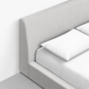 Close-up of a modern bed with a light grey fabric headboard and two white pillows on a neatly made bed, set against a white wall and light-colored floor.