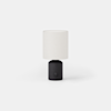 A cylindrical table lamp with a dark base and a light-colored drum shade.