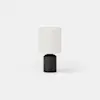 A cylindrical table lamp with a dark base and a light-colored drum shade.