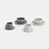 Four sets of minimalist cups and bowls with matching saucers in shades of grey and beige, arranged on a white background.