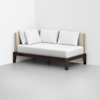 Minimalist daybed with a dark wooden frame, beige upholstered backrest, and three white pillows, placed in the corner of a white room with a light grey floor.