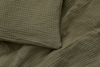 A close-up of a textured, olive green fabric with a crinkled, grid-like pattern, showing part of a pillow and a blanket.